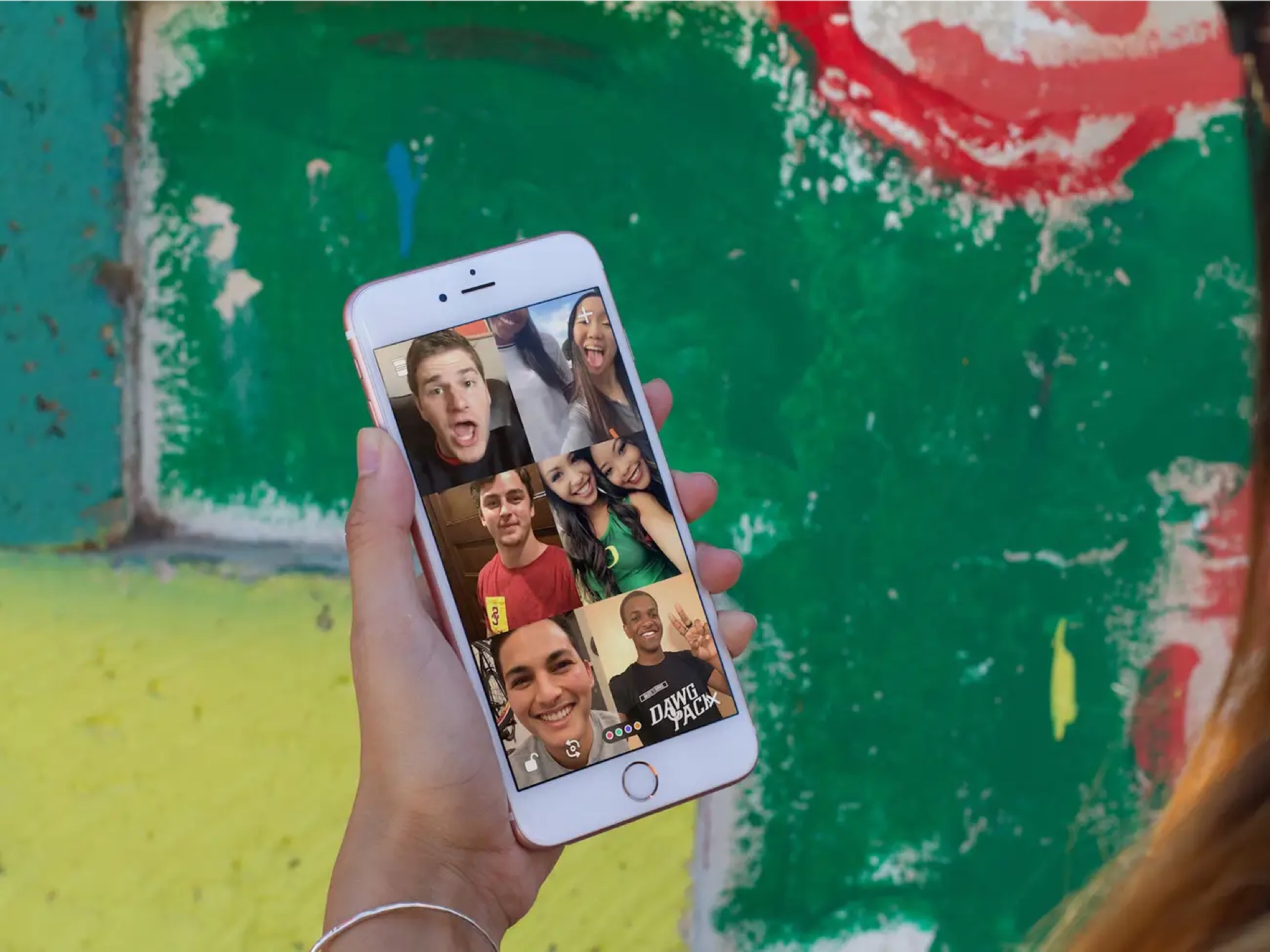 A hand holding a phone showing six friends on video together in a Houseparty room